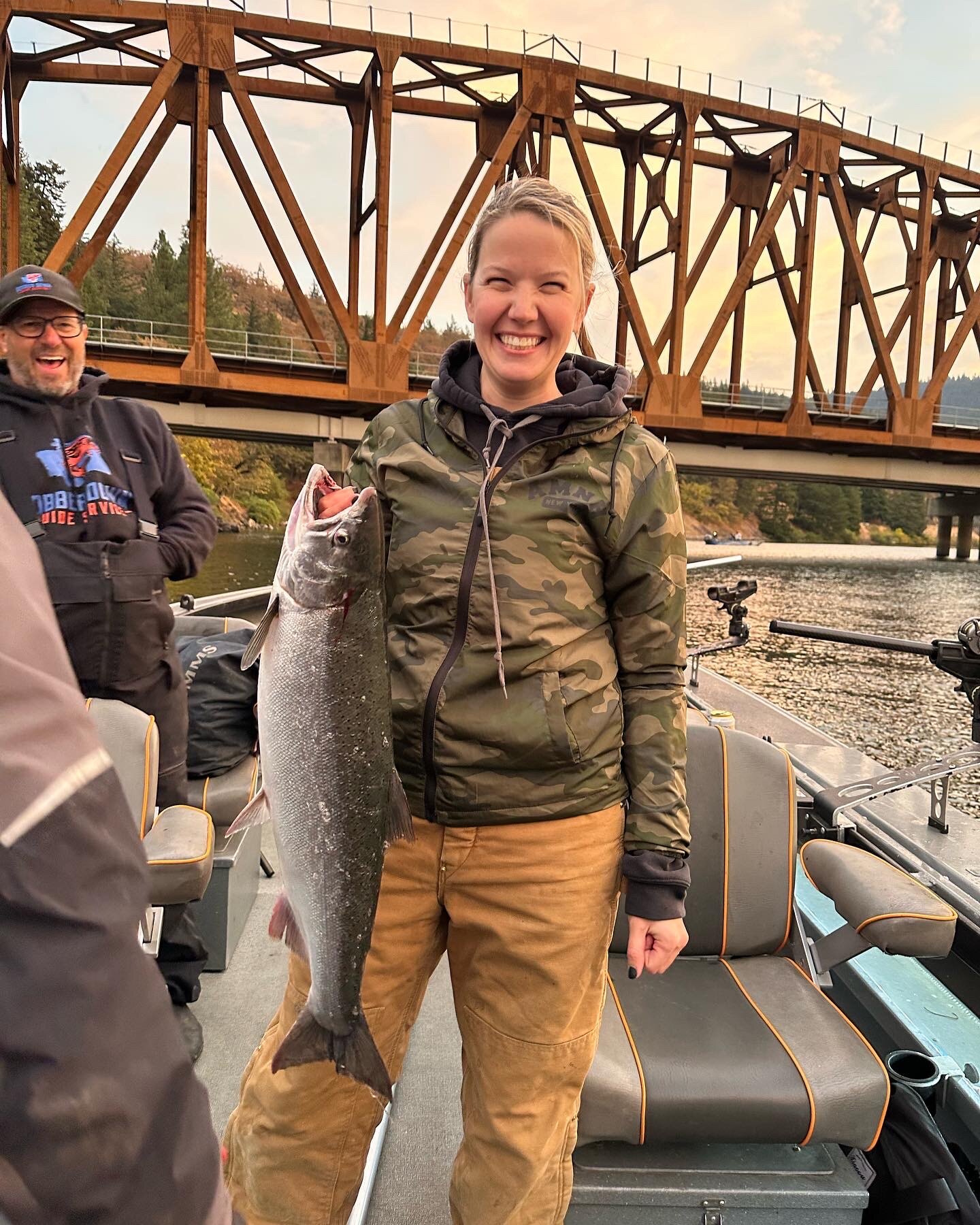 Smiling angler holding a coho salmon on the boat under a railroad bridge